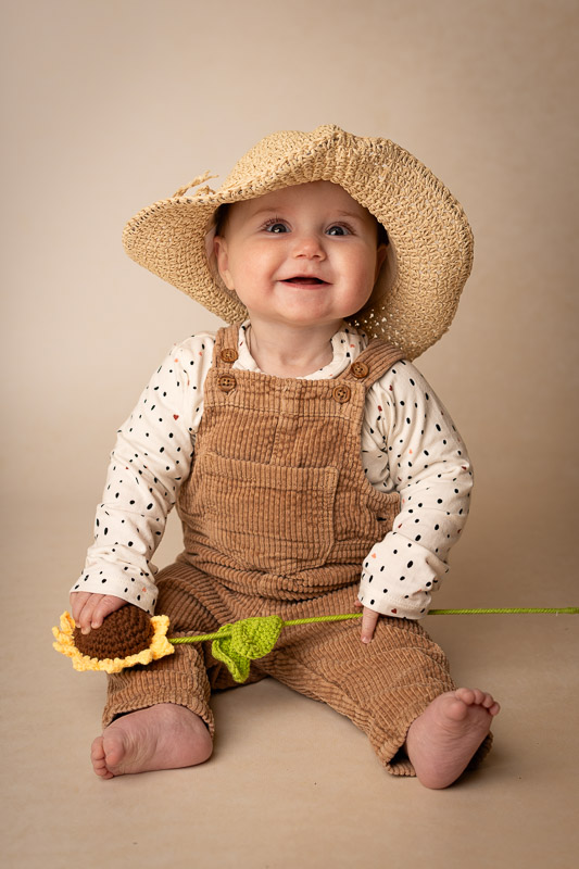 Portret-meisje-zonnebloem-sittershoot Portretfoto in de studio van Studio Suilen, van een meisje die zit met een zonnebloem voor een beige achtergrond. Sittershoot foto.